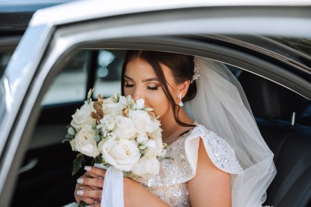 Mariée en robe blanche assise dans une voiture de cérémonie avec son bouquet