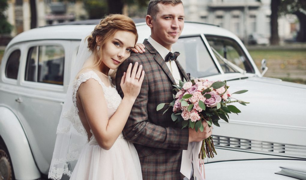 Mariés heureux qui posent devant une voiture ancienne avant la cérémonie de mariage