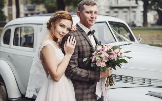 Mariés heureux qui posent devant une voiture ancienne avant la cérémonie de mariage