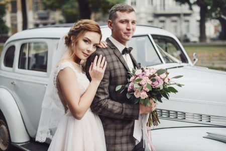 Mariés heureux qui posent devant une voiture ancienne avant la cérémonie de mariage