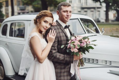 Mariés heureux qui posent devant une voiture ancienne avant la cérémonie de mariage