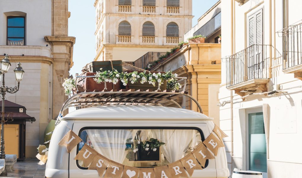 Van vintage jaune avec une pancarte Just Married devant un village pittoresque