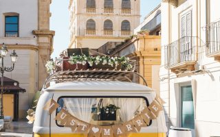 Van vintage jaune avec une pancarte Just Married devant un village pittoresque