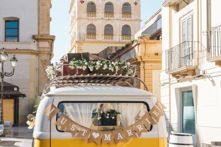 Van vintage jaune avec une pancarte Just Married devant un village pittoresque