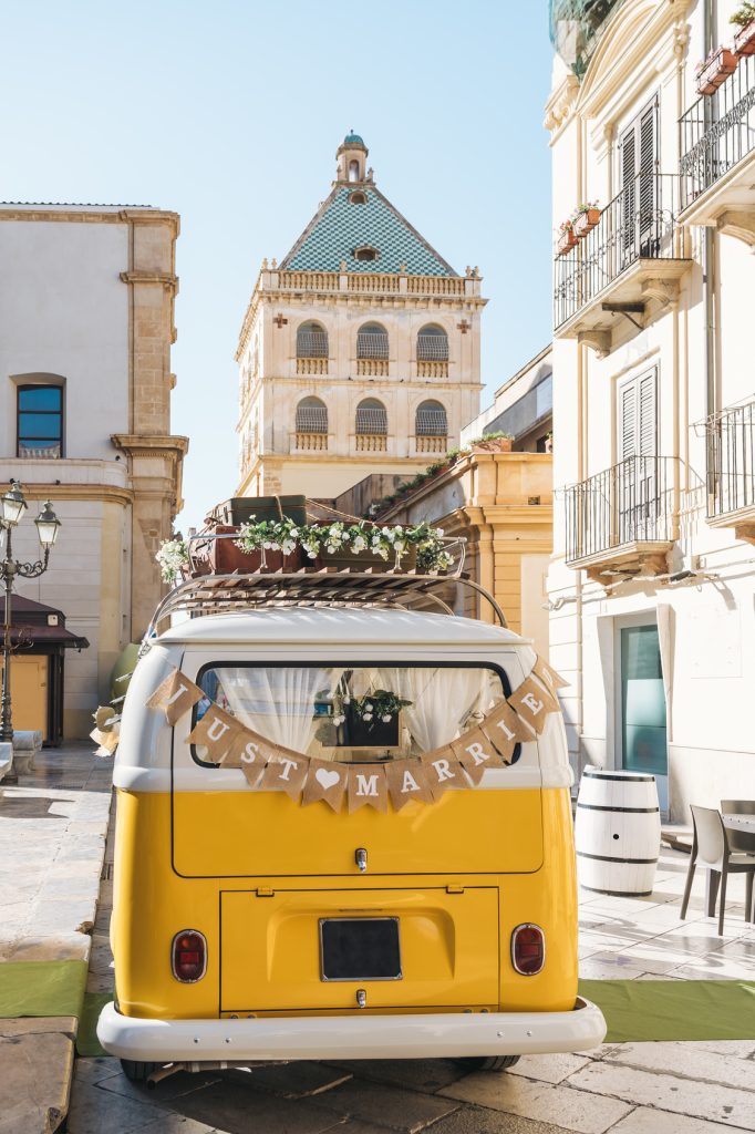 Van vintage jaune avec une pancarte Just Married devant un village pittoresque