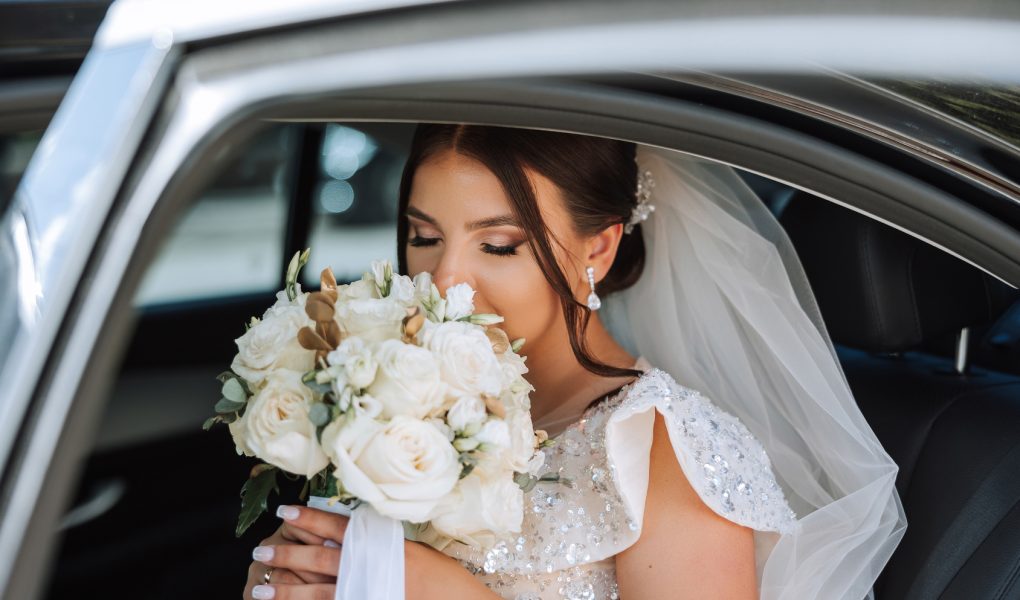Mariée avec son bouquet à l'arrière d'une voiture de cérémonie noire