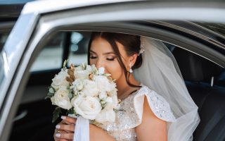Mariée avec son bouquet à l'arrière d'une voiture de cérémonie noire