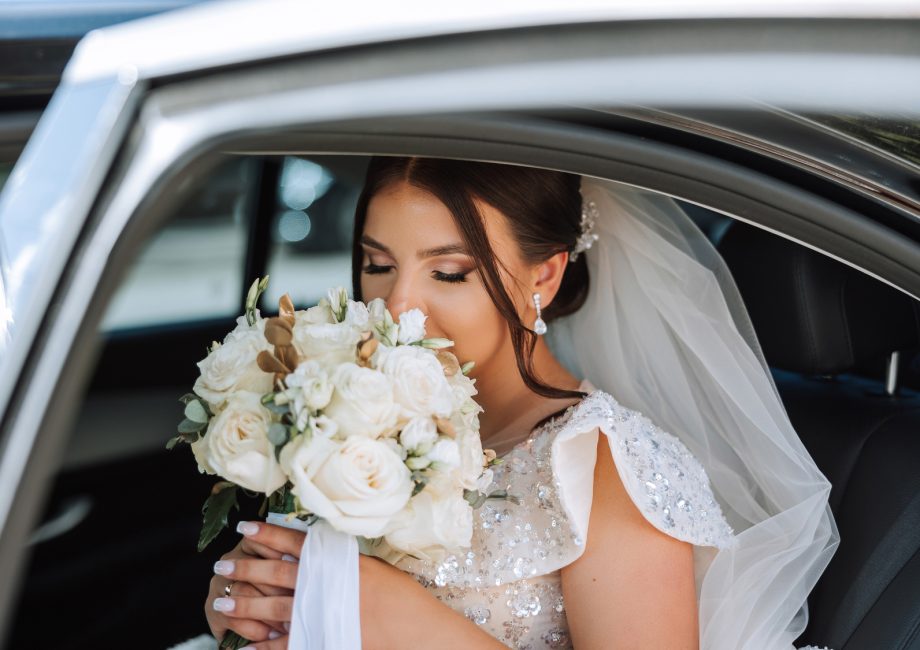 Mariée avec son bouquet à l'arrière d'une voiture de cérémonie noire