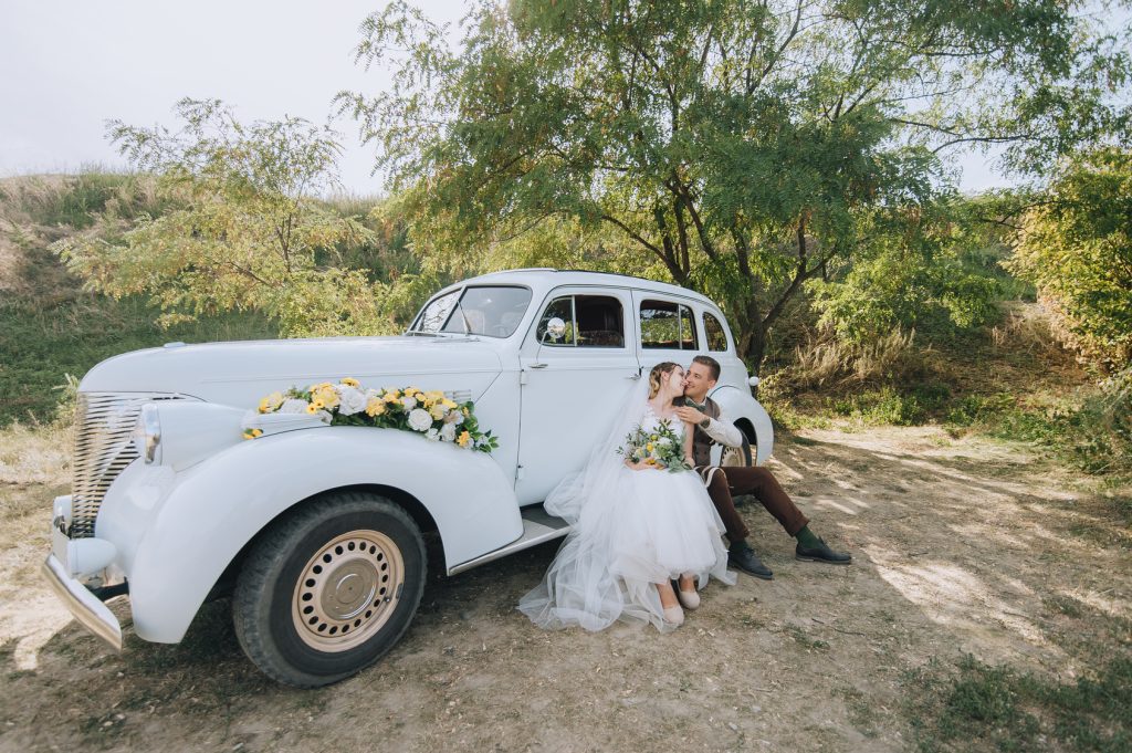 Mariés enlacés près d'une voiture classique le jour du mariage