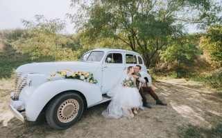 Mariés enlacés près d'une voiture classique le jour du mariage