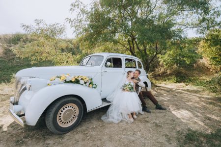 Mariés enlacés près d'une voiture classique le jour du mariage