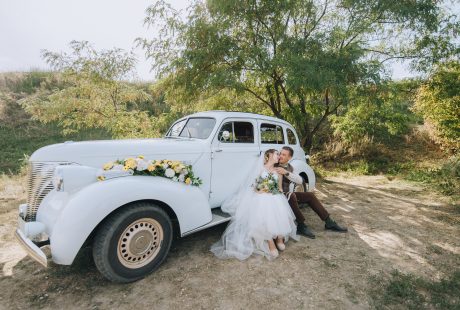 Mariés enlacés près d'une voiture classique le jour du mariage
