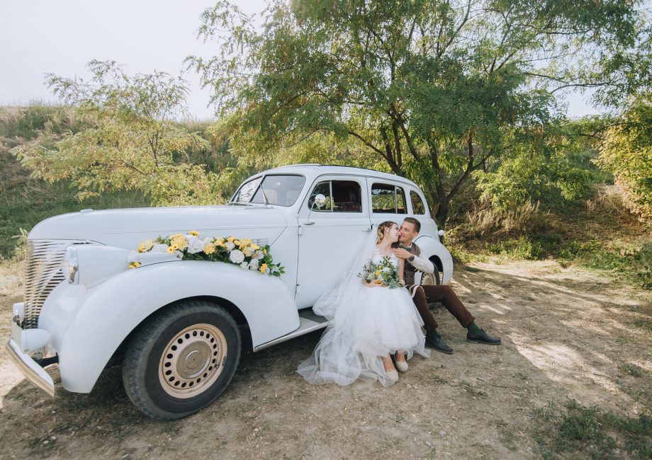 Mariés enlacés près d'une voiture classique le jour du mariage